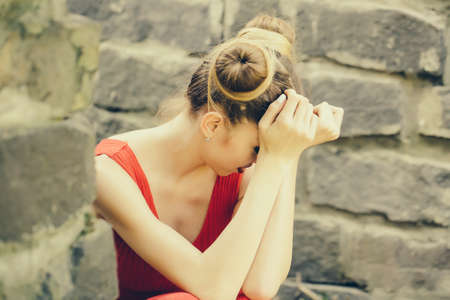 Beautiful sad young woman on a stone wall background posing hiding face in handsの写真素材