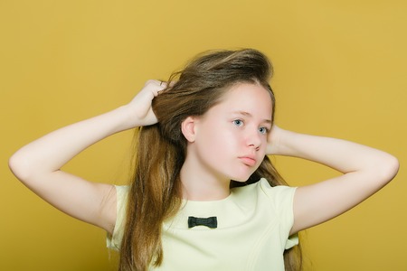 Teen girl with pretty face and long hair posing in studio on yellow background