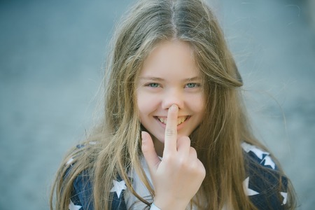 Beautiful young girl with long hair and finger on nose with smiling face outdoor closeupの写真素材