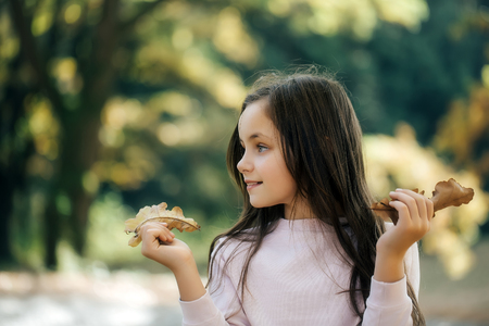 Beautiful girl preteen brunette with smiling cheerful face holding yellow leaves posing in forestの写真素材