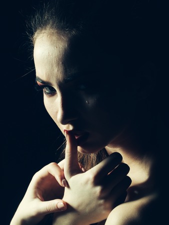 Young crying woman with bare shoulders holding hands near lips with tear on face on dark backgroundの写真素材