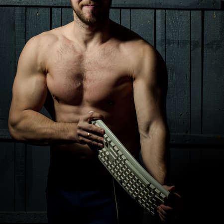 Young man with muscular body holding computer keyboardの写真素材