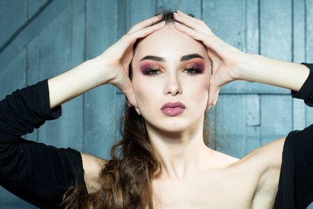 Beautiful woman model with bright makeup and hairstyle holding hands on head closeup in studio on wooden backgroundの写真素材