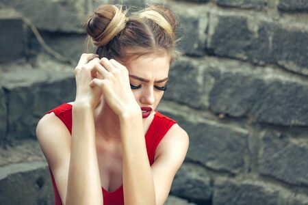 Beautiful sad young woman on a stone wall background posing with red lipsの写真素材