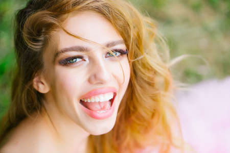 Beautiful woman with long blonde curly hair and red lips on happy smiling face outdoorの写真素材