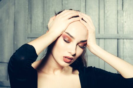 Beautiful woman model with bright makeup and hairstyle holding hands on head with closed eyes closeup in studio on wooden backgroundの写真素材