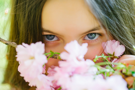 Beautiful small girl with brunette hair and smiling face in spring pink flower blossom sunny day closeupの写真素材