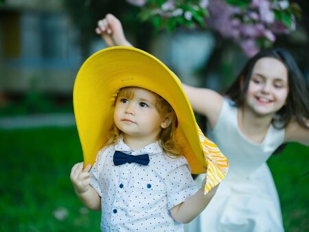 Small children of girl in white dress and boy in round yelloow hat and shirt with smiling face in spring on green grassの写真素材