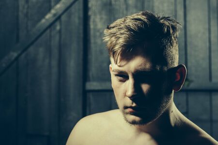 Handsome young macho man with bare chest and short stylish hair in studio on wooden backgroundの写真素材