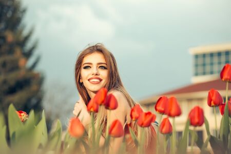 happy beautiful young slender girl is sitting with red tulipsの写真素材