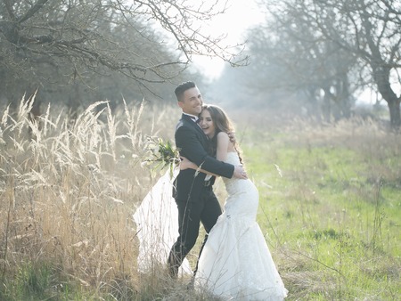 Young newlywed couple of woman in wedding dress and man walking in field in sunlight outdoorの写真素材