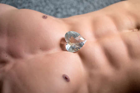 Athletic male bare torso with muscular belly abdominal muscles closeup with big diamond stone in...