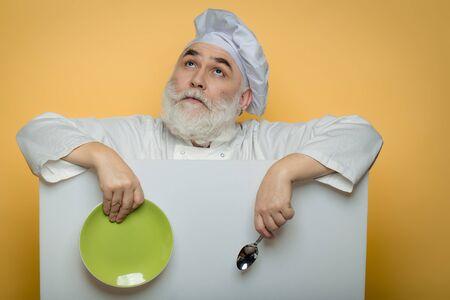 Happy bearded cook holding blank paper with spoon bottle and napkin on yellow background, copy spaceの写真素材