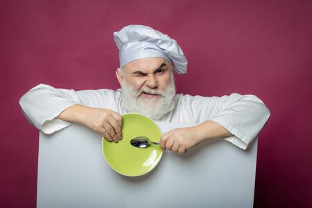 Happy bearded cook holding blank paper with spoon bottle and napkin on yellow background, copy spaceの写真素材