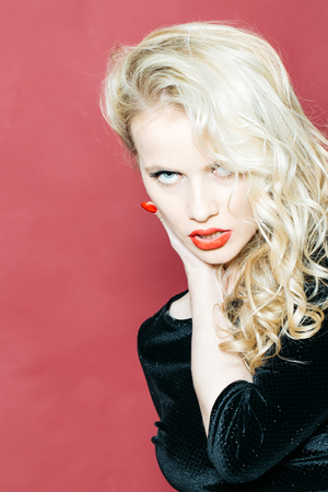 Sexy young woman with pretty face and blonde curly hair with red lips closeup on pink backgroundの写真素材