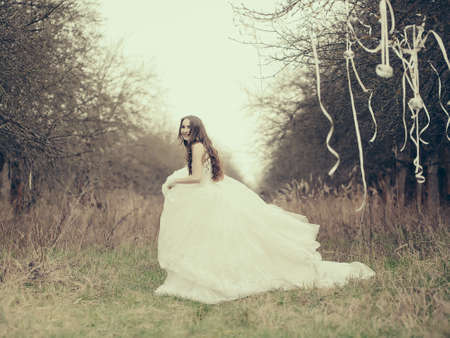 Happy bride with in white wedding dress dancing outdoor near trees with decorative ribbonsの写真素材
