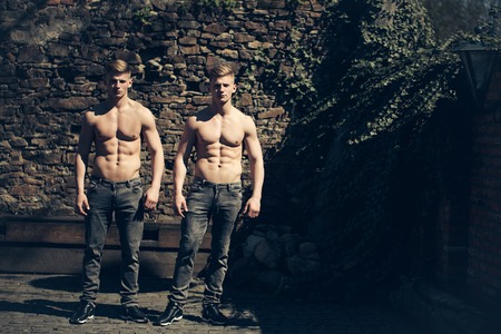Twin young sexy strong men models brothers bare-chested in jeans stand outdoor on mural backgroundの写真素材