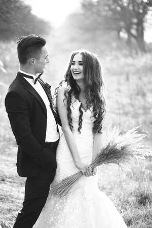 Happy newlywed couple posing and smiling in wedding dress and suit with flowers in field outdoor, black and whiteの写真素材