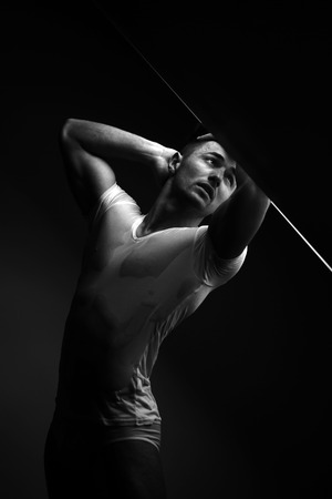 Sexy young man with muscular body in wet shirt posing in trunks near window, black and whiteの写真素材