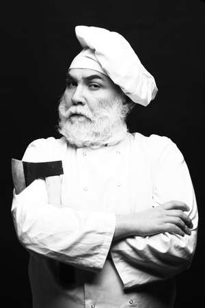 Bearded man cook in chef hat with sharp axe in studio on black background, black and whiteの写真素材