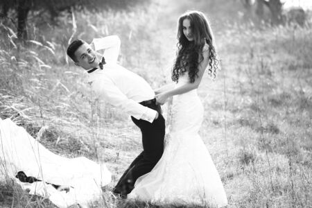 Young happy wedding couple of pretty woman and man undressing in field outdoor, black and whiteの写真素材