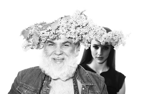 Middle-aged man with grey beard smiles with young woman in blurred background with lilac wreathes on...