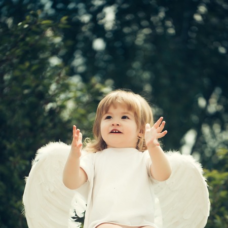 Happy cupid on the chair. Little boy in angel costume claps in hands