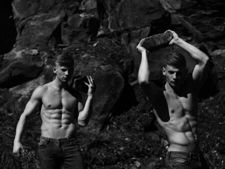 Strong men young handsome twins with sexy muscular body bare torso hold stones black and white on mountain backgroundの写真素材