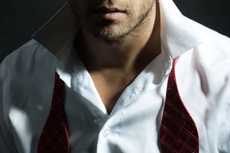 Sexy man with unshaven face in white shirt and red untied bow closeup