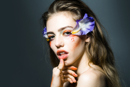 Young girl with pretty face and bright orange floral makeup with flowers blue petals in studio on grey backgroundの写真素材
