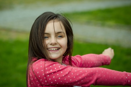 Smiling face of little cute happy girl child with blue eyes and brunette hair outdoor closeup on blurred green backgroundの写真素材