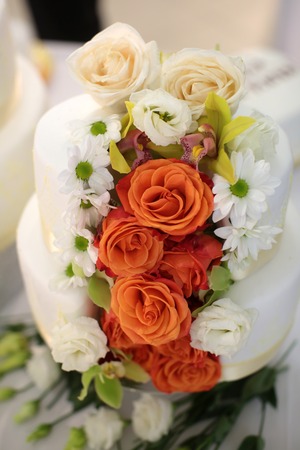 Wedding cake traditional multi level white beautiful decorated with roses and flowers on table backgroundの写真素材