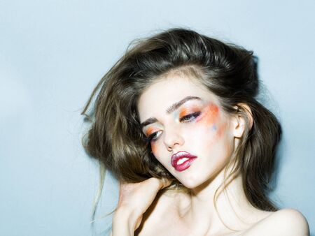 Young girl with hands near pretty face and bright orange makeup in studio closeupの写真素材