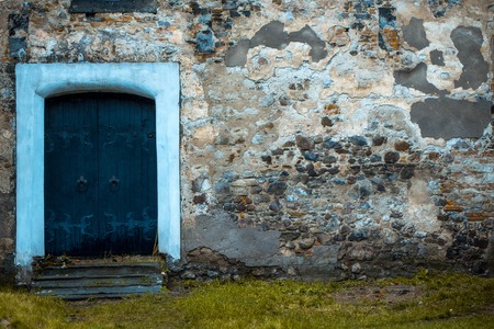 Old blue wooden door in stony building with textured wall and green grass background, copy spaceの写真素材