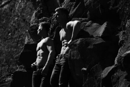 Strong torso of twin men shirtless in jeans with muscular body pose outside black and white on...