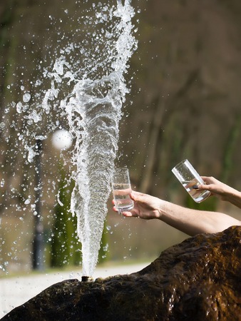 Human hands with water glasses near fountain in wet stone sunny day outdoorの写真素材
