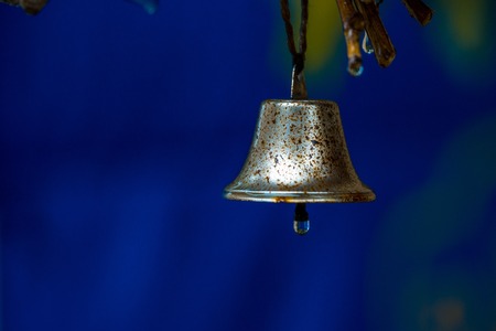 Rusty bell wet with drop of rain on clapper hangs on tree on blue background