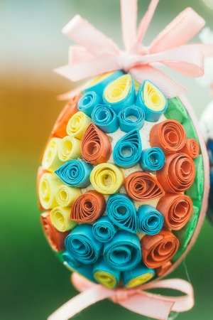 Easter egg decorated with colorful paper and pink ribbon bows in quilling on blurred background