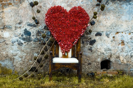 Floral arrangement with red rose flowers in shape of heart on chair outdoor on stony wall backgroundの写真素材