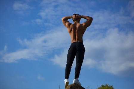 young macho man model athlete with muscular sexy body and bare back posing outdoor on sky backgroundの写真素材