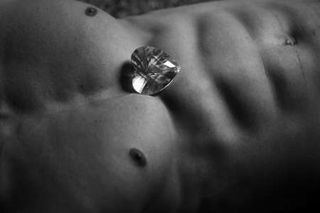 Athletic male bare torso with muscular belly abdominal muscles closeup with big diamond stone in shape of heart, black and whiteの写真素材