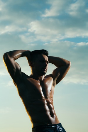 young macho man model athlete with muscular sexy body and wet bare chest outdoor on sky background
