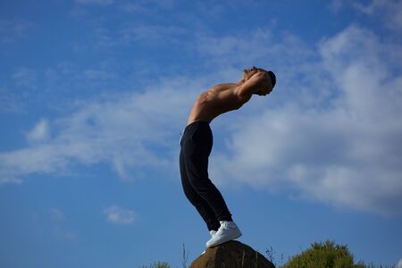 young macho man model athlete with muscular sexy body and bare chest posing outdoor on sky backgroundの写真素材