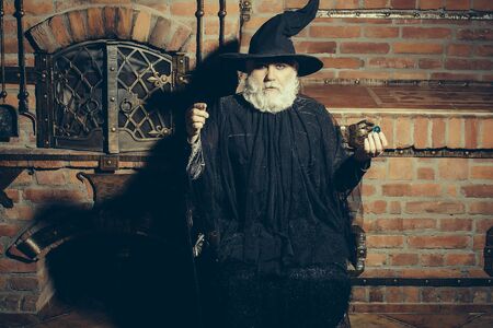 Old wizard in black costume and hat for Halloween on kitchen backgroundの写真素材