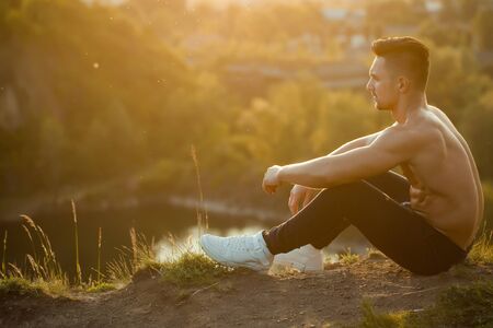 young macho man model athlete with muscular sexy body and bare chest outdoor sitting on ground sunny dayの写真素材