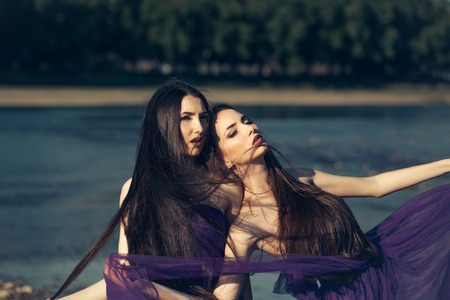 young pretty women with long windy hair in elegant violet dresses sunny day outdoor on natural backgroundの写真素材