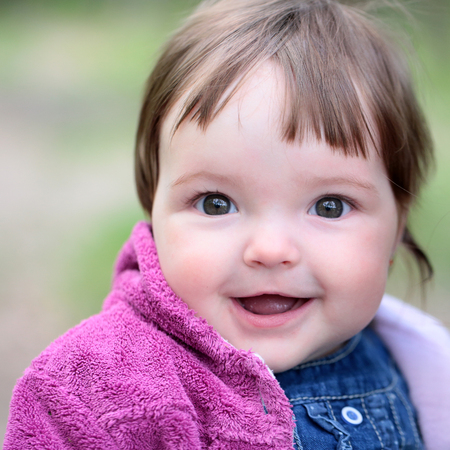 Small cute baby girl with pretty smiling face and funny eyes sunny day outdoor on natural background...