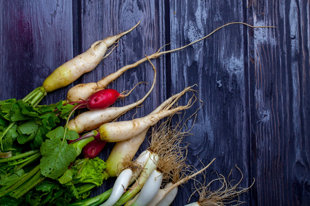 Bunch of fresh green onions and red white radishes on wooden table backgroundの写真素材