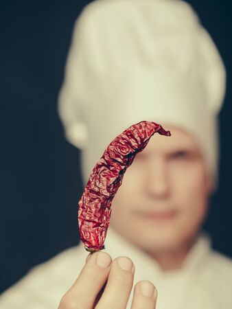 chef with a red chili pepper in his hands in white uniform and hat on black backgroundの写真素材