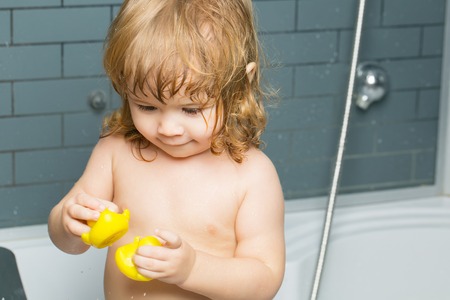Small cute funny baby boy with blonde hair playing with rubber yellow duckling toy in bath water